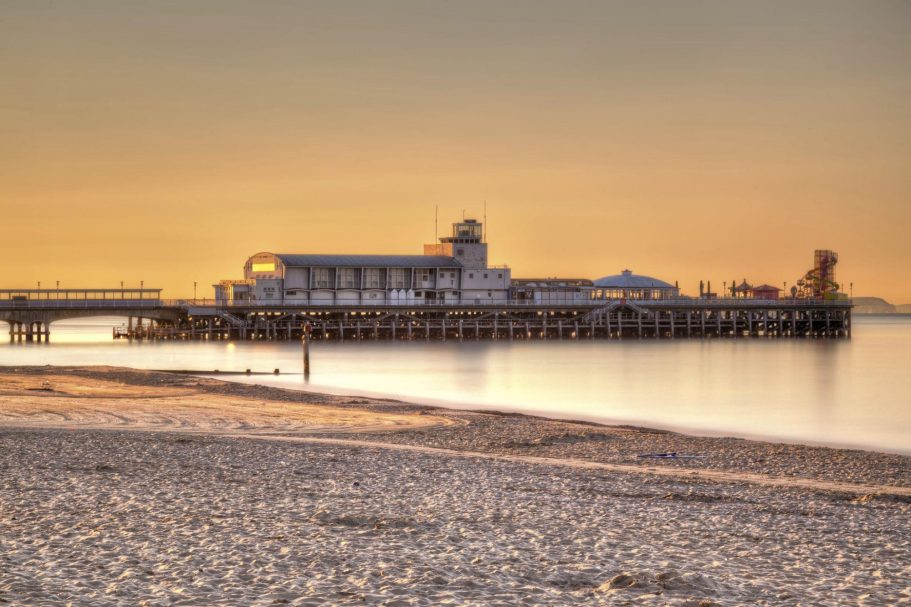 Bournemouth | Direct Cremations Pier at sunset with calm waters and a sandy beach in the foreground.