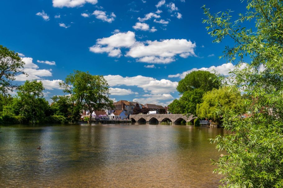 Fordingbridge | Direct Cremations Scenic riverside view with a bridge and lush greenery under a blue sky with clouds.